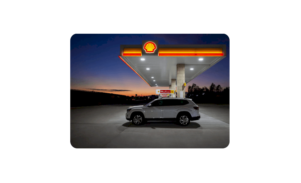 Car parked in front of Shell gas station at dusk.