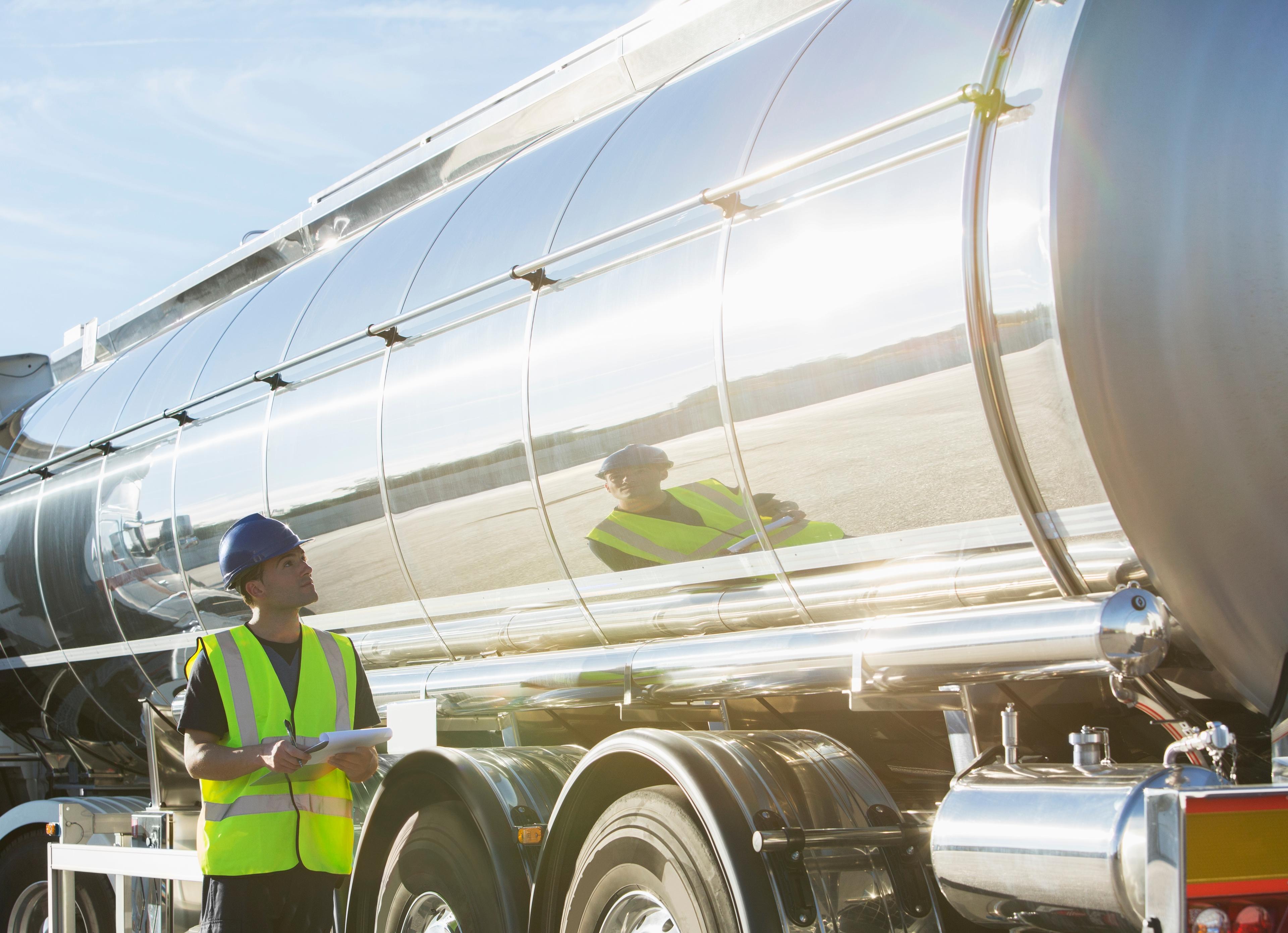 A man in a hard hat and reflective vest examines a fuel truck.