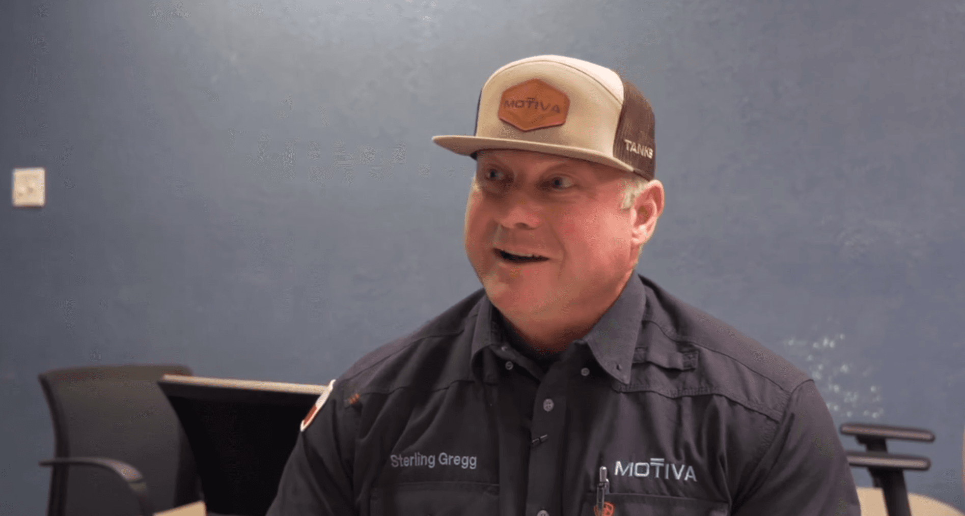 A man with a Motiva hat looks past the camera in a conference room.