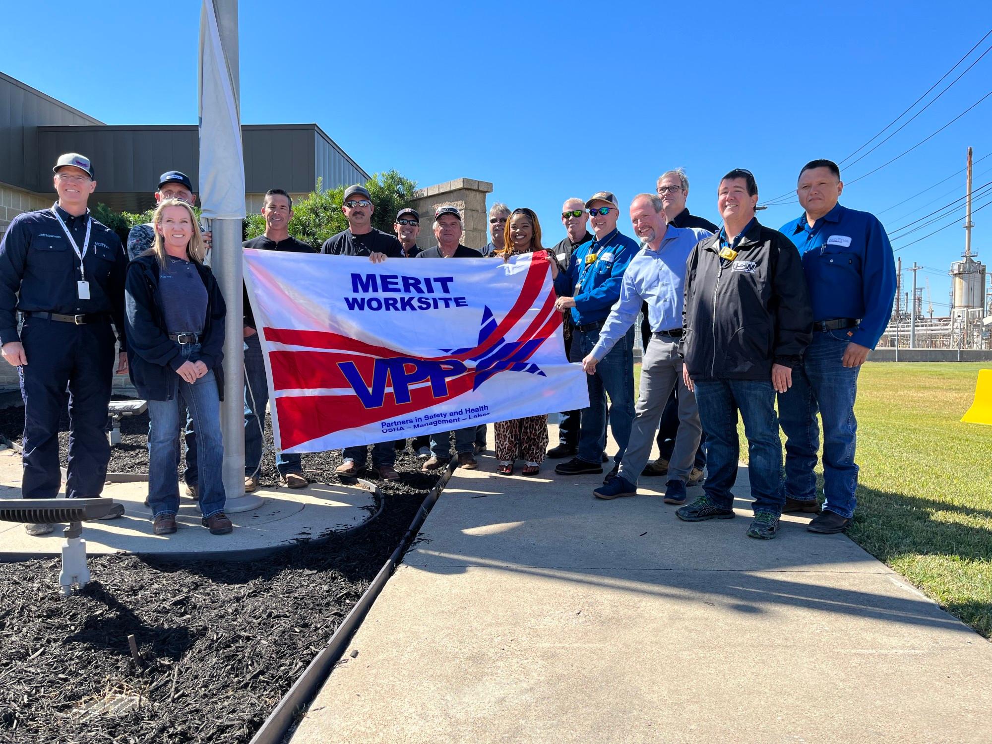 A group of Motiva employees hold up a VPP Merit Worksite flag at the Motiva refinery.