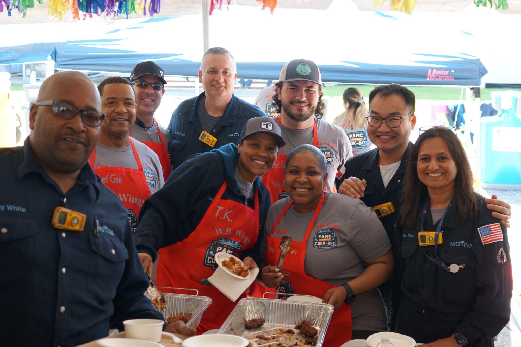 A group of people smiling and holding food at a cook-off.